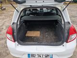 une petite voiture blanche dont le coffre est ouvert, garée sur la route