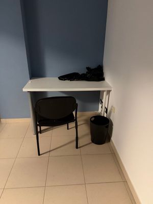 a desk with a chair and a trash can in the corner of the room