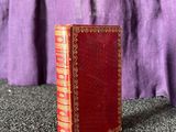 an old red book sitting on top of a table next to a purple curtain