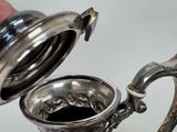 a person holding a silver tea pot with a handle