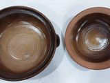 two brown ceramic bowls sitting next to each other on a white surface