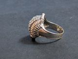 a silver ring with a shell on it on a black surface