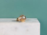 un gros plan d'une bague en or sertie d'un diamant, posée sur un bloc de marbre