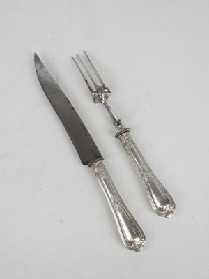 une paire de couteaux plaqués argent et un couteau posés sur une surface blanche