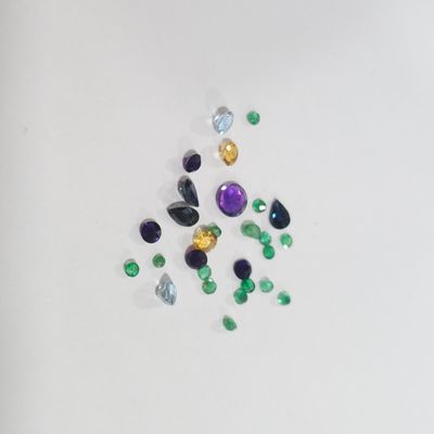 Plusieurs pierres précieuses de différentes couleurs sont dispersées sur une surface blanche.