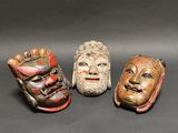 three wooden masks are sitting on a table with a black background