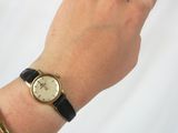 wrist shot of a woman wearing a gold watch and black leather bracelet