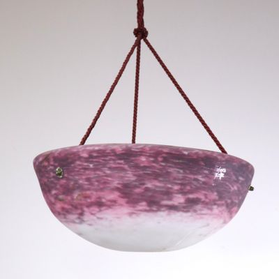 un bol en verre violet et blanc suspendu à une corde sur un mur blanc