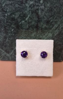 une paire de boucles d'oreilles en pierre violette posées sur un tissu blanc