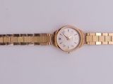 une image représentant une montre en or avec un cadran blanc posée sur une surface blanche