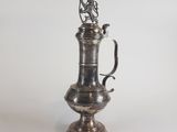 une cafetière ancienne en métal argenté, surmontée d'un oiseau