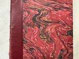 un cahier marbré rouge et noir posé sur une table blanche