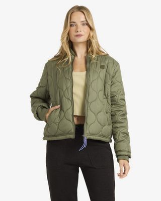 une femme vêtue d'une veste matelassée verte et d'un pantalon noir