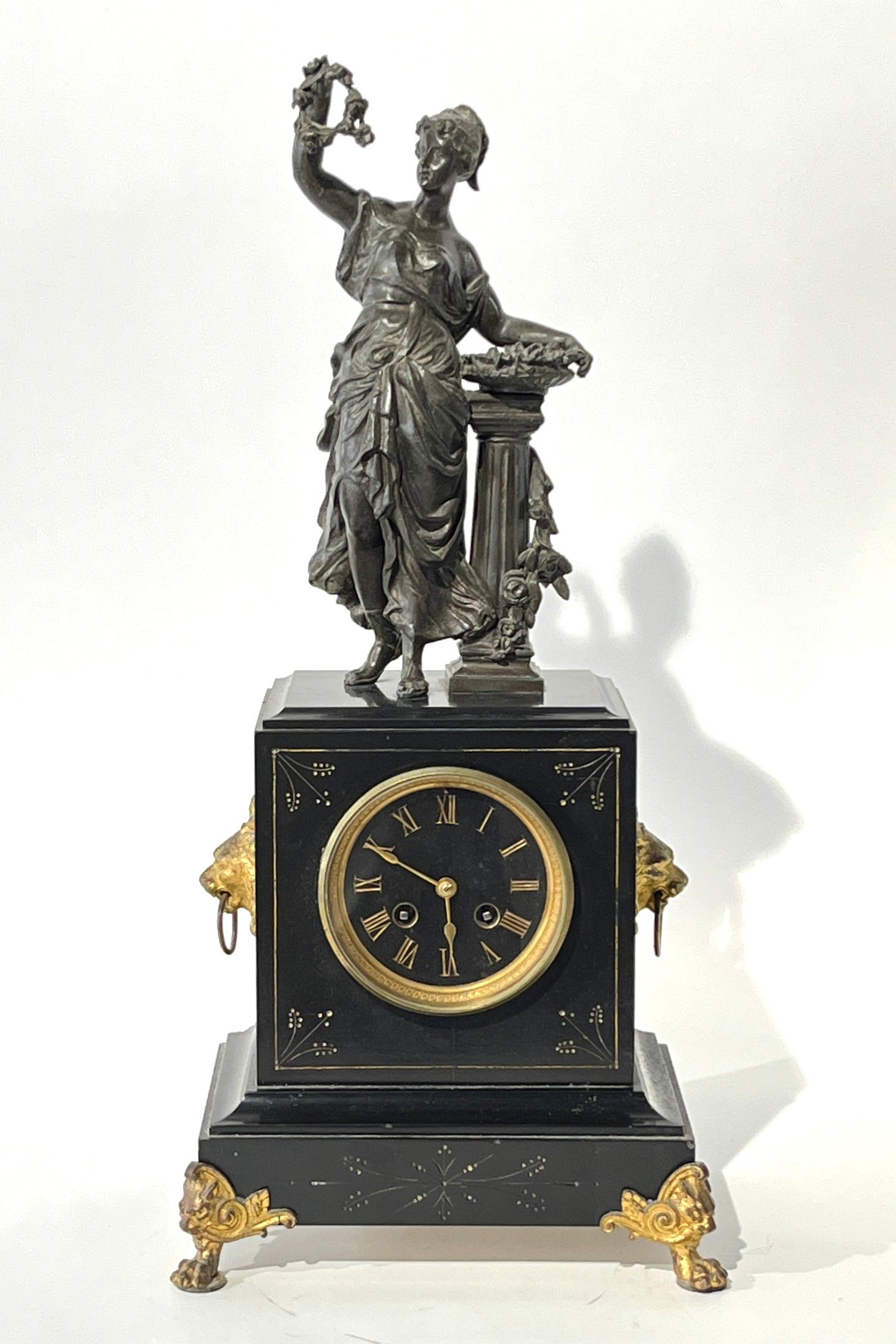 Pendule à poser en marbre noir et régule à décor d'une élégante à la corbeille de fleurs. Fin du XIXe siècle. H. 54 c...