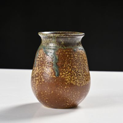 un vase marron posé sur une table sur fond noir
