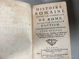 Quelqu'un tient un vieux livre ouvert sur une table, à côté d'une pile de livres.