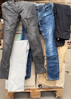 Plusieurs paires de jeans sont empilées sur une palette devant un bâtiment