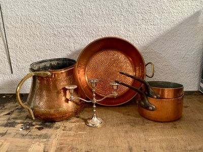 Plusieurs casseroles et poêles en cuivre sont posées sur une table en bois