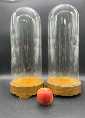 deux cloches en verre avec un socle en bois et une pomme rouge