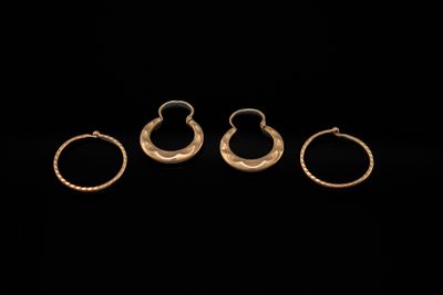 trois bagues en or et une paire de boucles d'oreilles sur fond noir