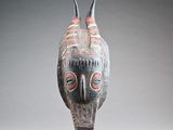 une image représentant un masque en bois posé sur un socle, sur fond gris