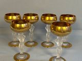 six verres à vin dorés, bordés d'or, posés sur une table blanche