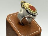 silver and gold ring with a red stone on top of a wooden block