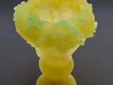 a yellow glass vase with a flower inside of it on a gray surface
