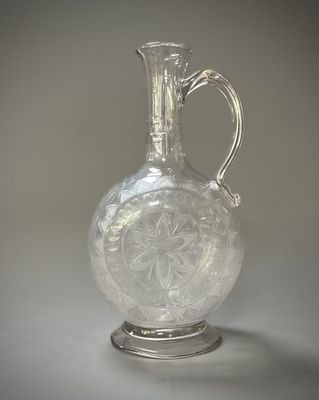 un vase en verre transparent muni d'une poignée en argent, posé sur une table