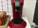 a red coffee maker sitting on a shelf next to a cup of coffee