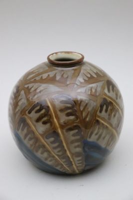 un vase brun et bleu posé sur une surface blanche