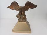 statue d'un aigle posée sur un socle, sur une surface blanche