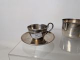 a silver cup and saucer sitting on a glass table