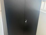 une armoire noire dans un coin de la pièce, près d'une fenêtre