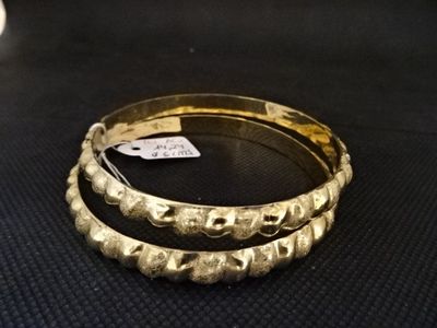 deux bracelets en or posés sur une surface noire, sur laquelle est fixée une étiquette