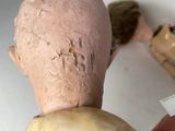 a hand holding a piece of paper next to a doll ' s head