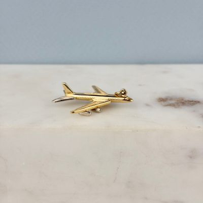 la breloque en forme d'avion en or repose sur une surface en marbre