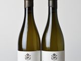 two bottles of white wine sitting on top of a wooden table