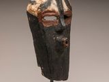 a close up of a wooden mask on a black stand