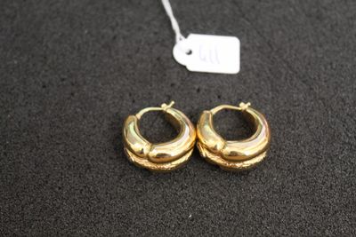 deux paires de boucles d'oreilles créoles en or posées sur une surface noire, accompagnées d'une étiquette de prix
