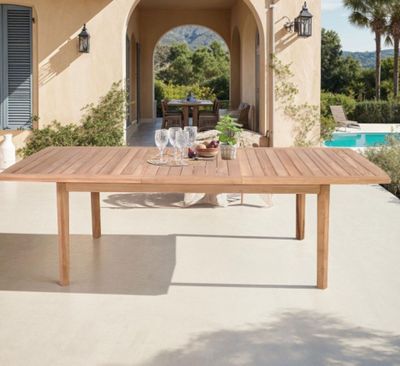 une table en bois sur une terrasse, avec un verre de vin posé dessus