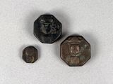 trois morceaux de métal sur lesquels est représenté un visage, posés sur une surface blanche