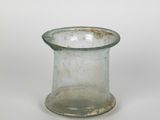 un petit vase en verre dont le bord est rouillé, posé sur une surface blanche