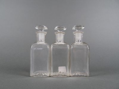 trois bouteilles en verre transparent posées sur une surface grise