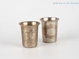 two silver cups with designs on them sitting next to each other
