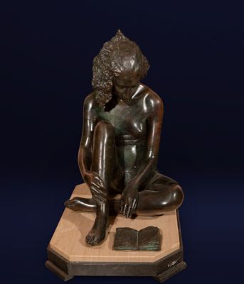 statue en bronze représentant un garçon assis sur un socle, un livre sur les genoux