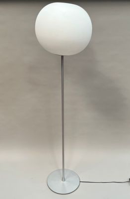 la lampe repose sur un pied métallique surmonté d'une boule blanche