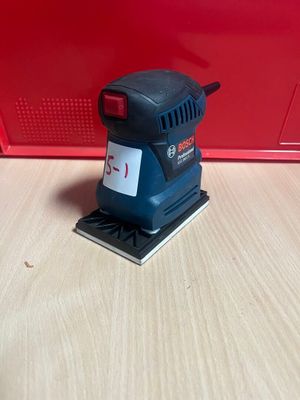 un gros plan d'une ponceuse posée sur une table, sur fond rouge