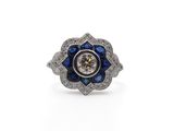un gros plan d'une bague ornée d'une fleur en diamants et saphirs sur fond blanc