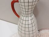 a white vase with a red handle sitting on a rug